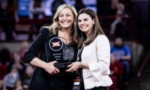 KJ Kindler smiles with a representative from hte Big 12 while receiving the 2021-22 Big 12 Coach of the Year award