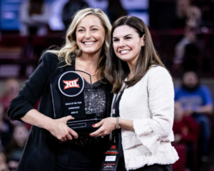 KJ Kindler smiles with a representative from hte Big 12 while receiving the 2021-22 Big 12 Coach of the Year award
