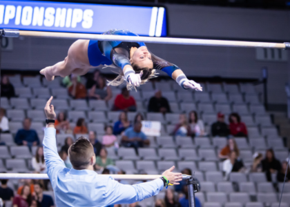Riley McCusker performs a Shaposh variation on bars while Owen Field stands by for safety