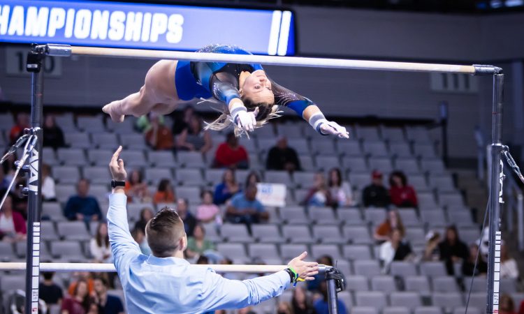 Riley McCusker performs a Shaposh variation on bars while Owen Field stands by for safety