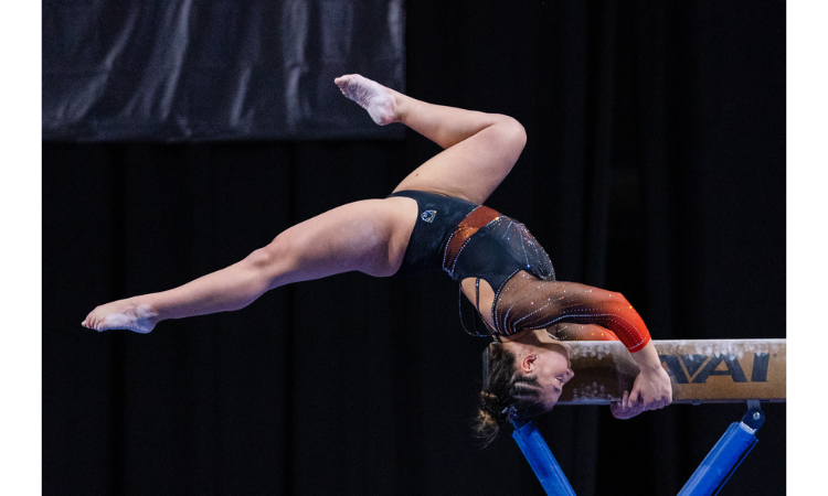 Sydney Gonzales does her beam mount where she is golding onto the beam and is upside down off the end