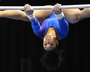 Sydney Barros grips the bars with her legs in a straddle and her head handing upside down