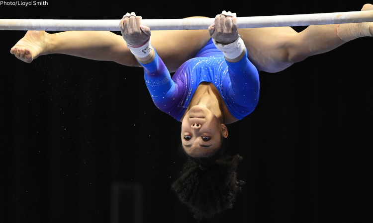 Sydney Barros grips the bars with her legs in a straddle and her head handing upside down