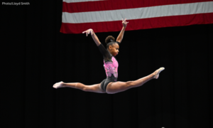 Kelsie Woolford in a split position in the air with the corner of the american flag visible behind her