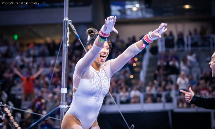 Kayla DiCello holds her stick after her bar routine. Her mouth is open and her tongue is slightly out in a smile.