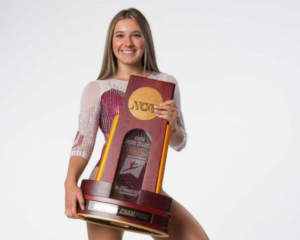 Mackenzie Estep poses in an Oklahoma leotard with a championship trophy