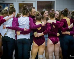 Texas Woman's gymnasts huddle together holding hands behind their backs