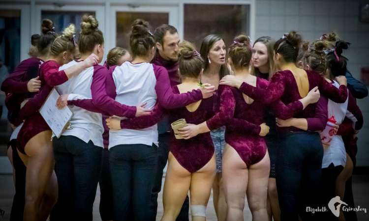 Texas Woman's gymnasts huddle together holding hands behind their backs