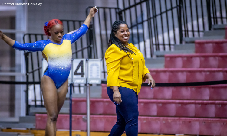 Corrinne Tarver smiles and stands next to a gymnast.