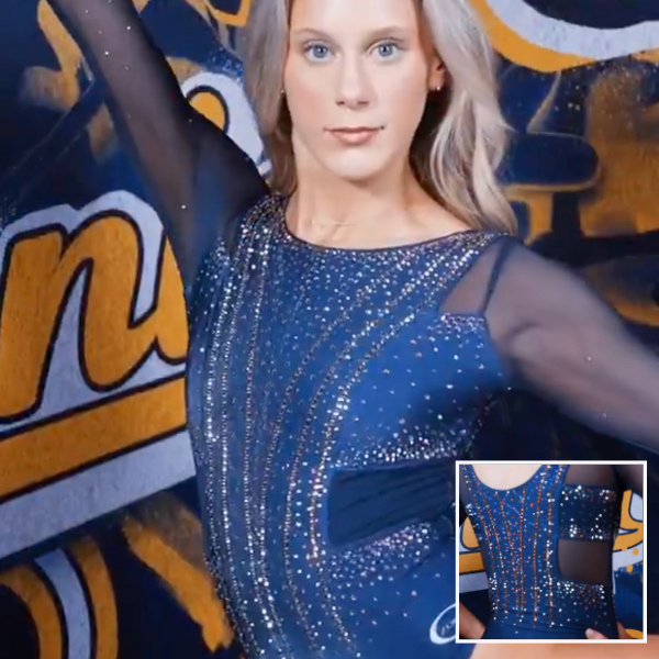 A gymnast is posing in a sleek navy leotard adorned with sparkling rhinestones in a symmetrical pattern across the front. The leotard has sheer sleeves and delicate rhinestone detailing, adding elegance to the design.