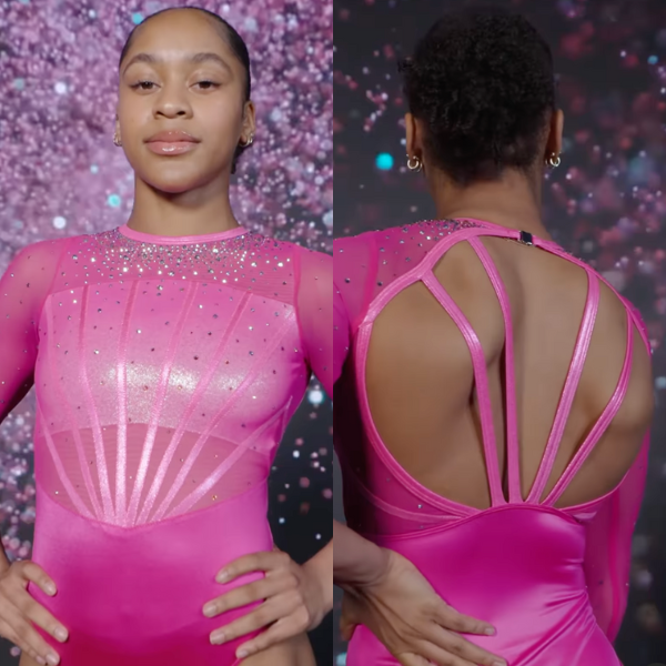 A Florida gymnast in a vibrant, hot pink leotard with sheer mesh sleeves. The front of the leotard has a fan-like design of silver rhinestones that radiate from the neckline down to the chest. The open back is framed by thin, shiny straps, creating a modern and dynamic design.