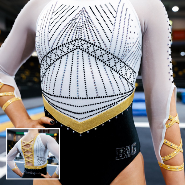 A gymnast in a black and gold leotard, with gold accents forming a v-shaped pattern on the chest. The design is enhanced by black and silver rhinestones and mesh sleeves that match the bold and elegant theme.