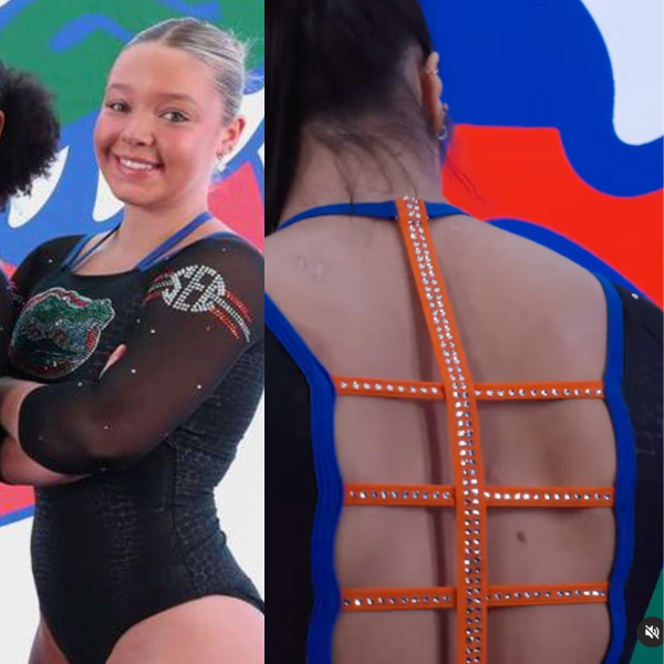 A gymnast wearing a black Florida Gators leotard with the team logo on the chest in green, blue, and orange. The leotard features orange straps along the back with blue trim and sparkling embellishments. The background features a large Florida Gators logo.