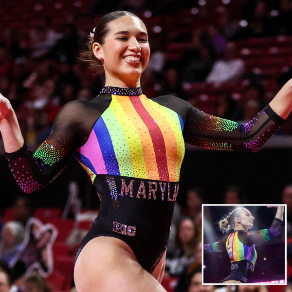 A gymnast from Maryland is performing in a black leotard with a bold rainbow stripe down the front. The leotard features sheer black sleeves with colorful rhinestones, and the word "Maryland" is visible in rhinestones near the gymnast's stomach.