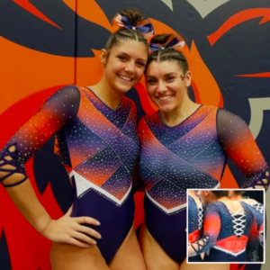 This image shows two gymnasts smiling while wearing matching leotards. The leotards feature a vibrant, geometric design with a color gradient of orange, red, and purple. The chest is adorned with scattered crystals in a symmetrical pattern. The sleeves are sheer and gradient from deep purple to orange, with small white crystals spread across the fabric. The lower half of the leotard is navy with a white zig-zag trim separating it from the upper design. The leotard has lace-up details on the sides of the sleeves, adding a unique touch. An inset image shows the back of the leotard, which has a crisscross lace-up detail in white, and the word "UTICA" printed on the lower back. Both gymnasts have matching ribbon bows in their hair that complement the leotard's color scheme.