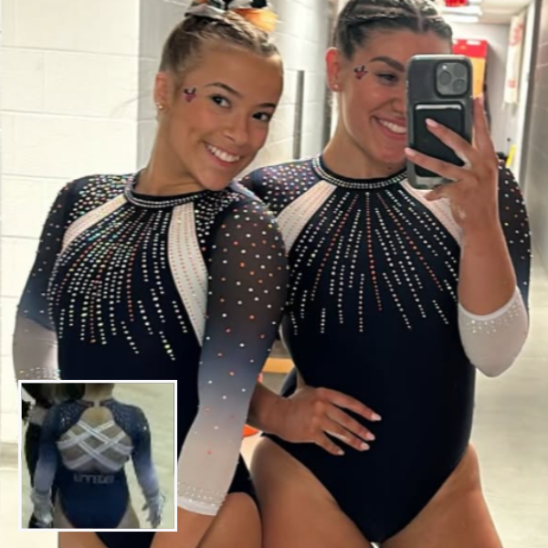 A gymnast in a white and navy blue leotard with geometric detailing and shimmering silver and orange rhinestones. The blue to white ombre sleeves have mesh accents and the back has a sporty crisscross strap design.