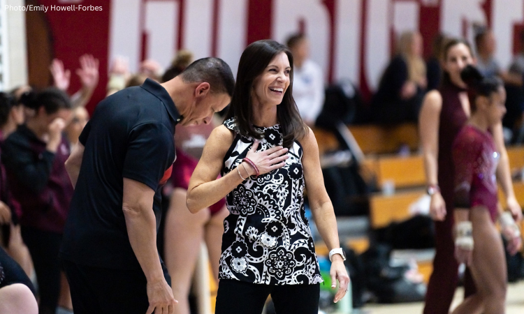 Coach Sara Carver-Milne stands with one hand over her chest on the sidelines