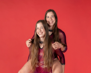 The Stallings twins stand together in leotards in front of an orange background