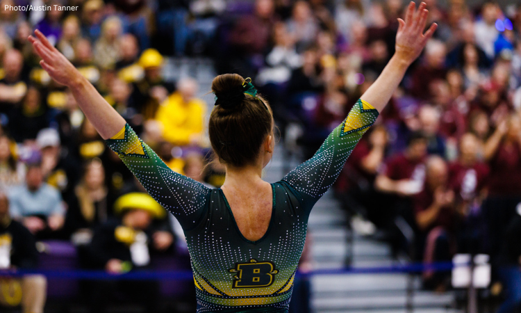 Brockport gymnast raising her arms in a salute after her routine