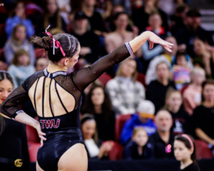 A gymnast poses on floor with the back of the TWU leotard visible.