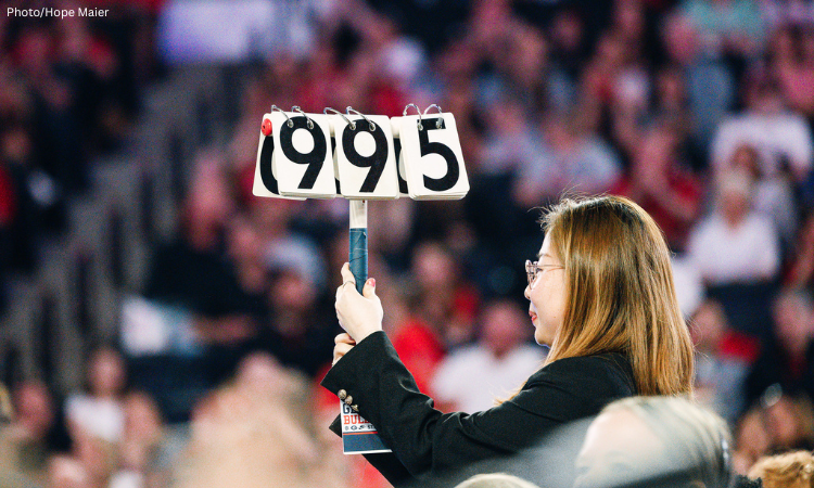 A woman holds up a 9.95 score card at a gymnastics meet.