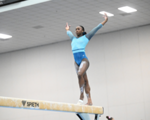 Zoey Molomo stands on the beam with arms up preparing for her next skill.