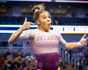 Oklahoma gymnast Danielle Sievers performs a dynamic floor routine, making an expressive face and pointing both hands outward during a choreographed moment.
