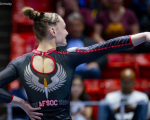 Maggie Slife poses on floor showing the back of her leotard with a large air force logo on the back