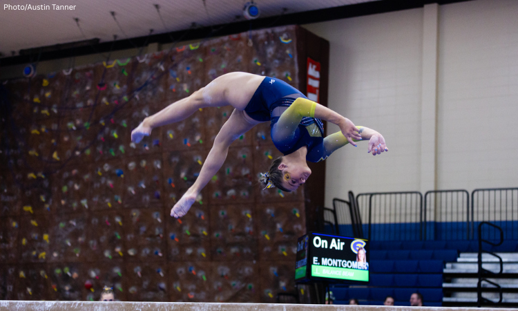 W–Eau Claire gymnast Ella Montgomery performs a backflip on balance beam, wearing a blue and yellow leotard, with a scoreboard in the background displaying her name.