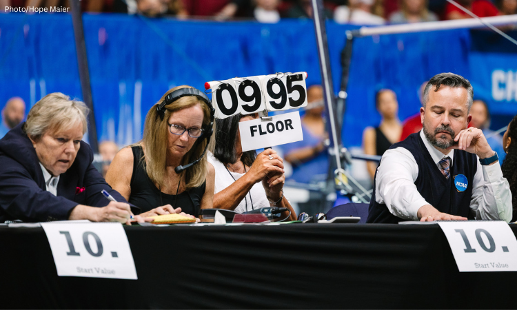 College women's gymnastics judges hold up a sign showing a 9.95 score given to an athlete
