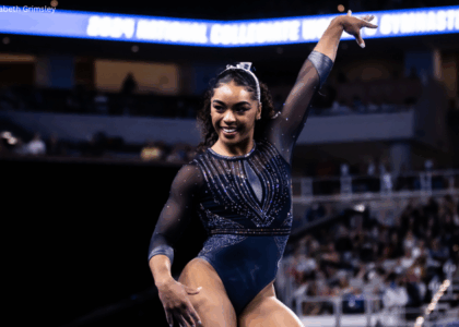 eMjae Frazier poses on floor exercise with one arm pointed up.
