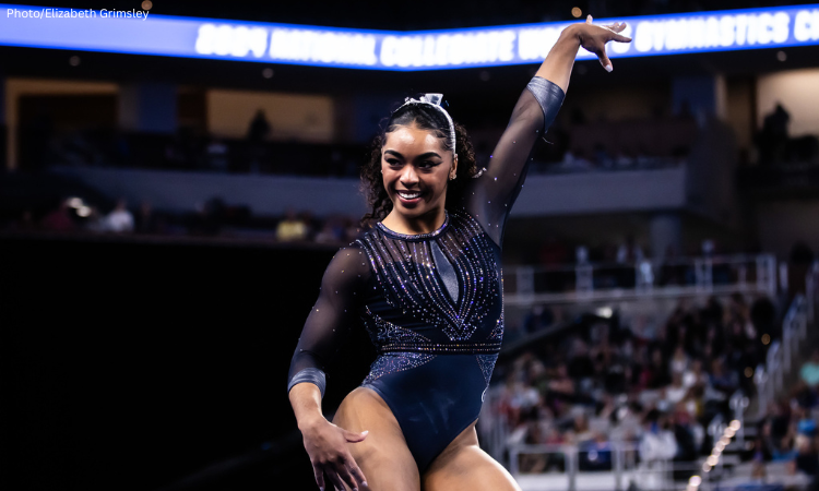 eMjae Frazier poses on floor exercise with one arm pointed up.