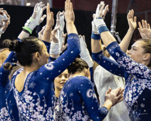 The GW gymnastics team huddles together and raises their hands