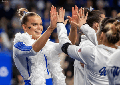 Creslyn Brose of Kentucky gives her teammates high fives. She is wearing the Kentucky celebratory feather boa draped over her shoulders.