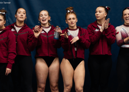 A team of gymnasts stands on the sidelines. Each gymnast has a unique facial expression