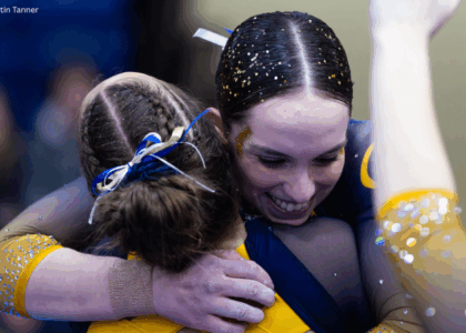 Two team members hug each other. The photo shows a closeup of their hair, which is covered in glitter