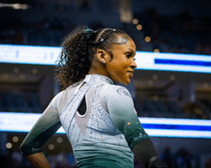 Nikki Smith poses on floor, showing the back of her green and white leotard with her head turned to show her profile