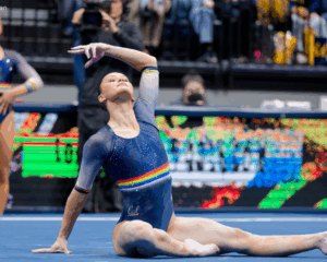 Tonya Paulsson poses while sitting on floor with one arm outstretched and one bend over her head.
