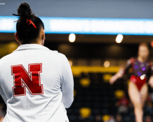 The photo shows a gymnasts back with a focus on a white jacket with the Nebraska logo.