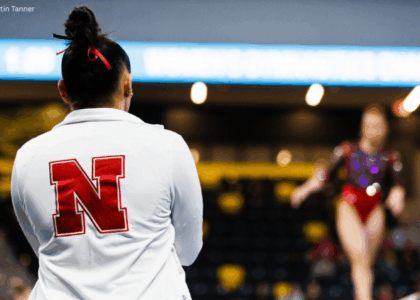 The photo shows a gymnasts back with a focus on a white jacket with the Nebraska logo.