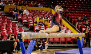 Reese Grolla of Arizona State poses sitting on beam with one leg extended.
