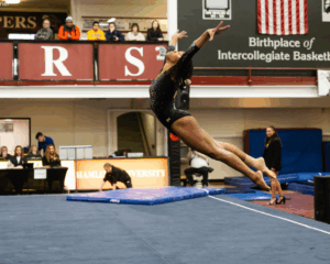 Reanna McGibboney of Oshkosh does an arched jump on floor with both arms up, head back, and legs extended behind her.
