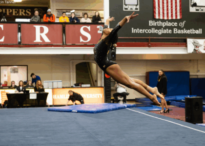 Reanna McGibboney of Oshkosh does an arched jump on floor with both arms up, head back, and legs extended behind her.