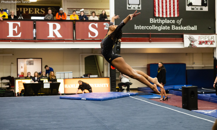 Reanna McGibboney of Oshkosh does an arched jump on floor with both arms up, head back, and legs extended behind her.