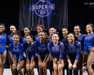 A photo of the Fisk gymnastics toeam together from 2023 in front of a Super 16 sign.