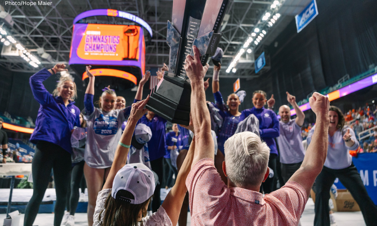Clemson coaches hold up ACC trophy while team celebrates in the background. 