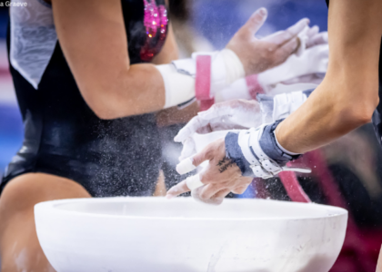 Two gymnasts stand by a chalk bucket chalking their grips.