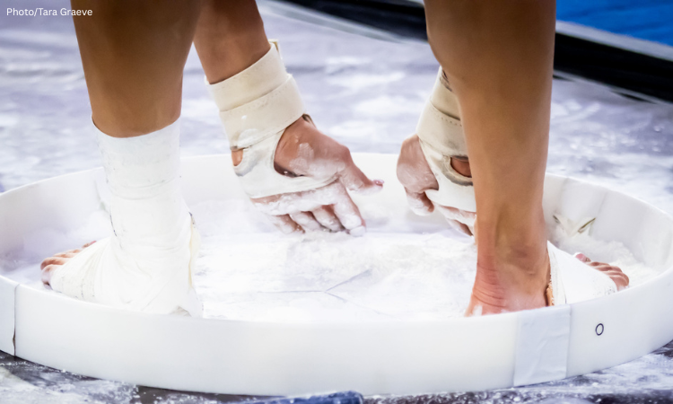 Close-up shot of gymnast chalking up in chalk bucket.