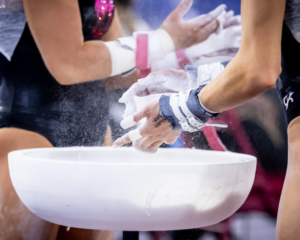 Two gymnasts chalk up during bars warmup
