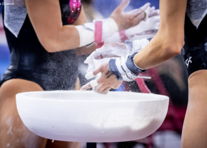 Two gymnasts chalk up during bars warmup